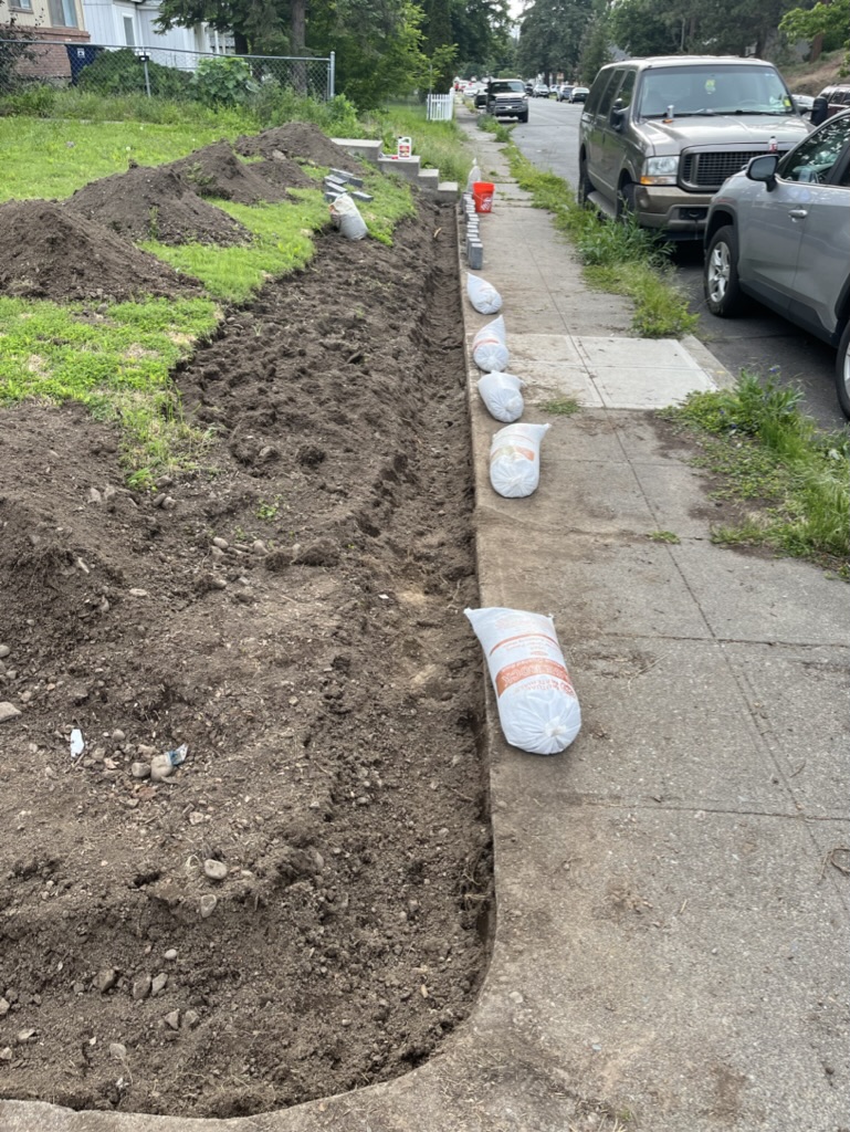 A ditch along the side walk that is preparation for a retaining wall in front of house.